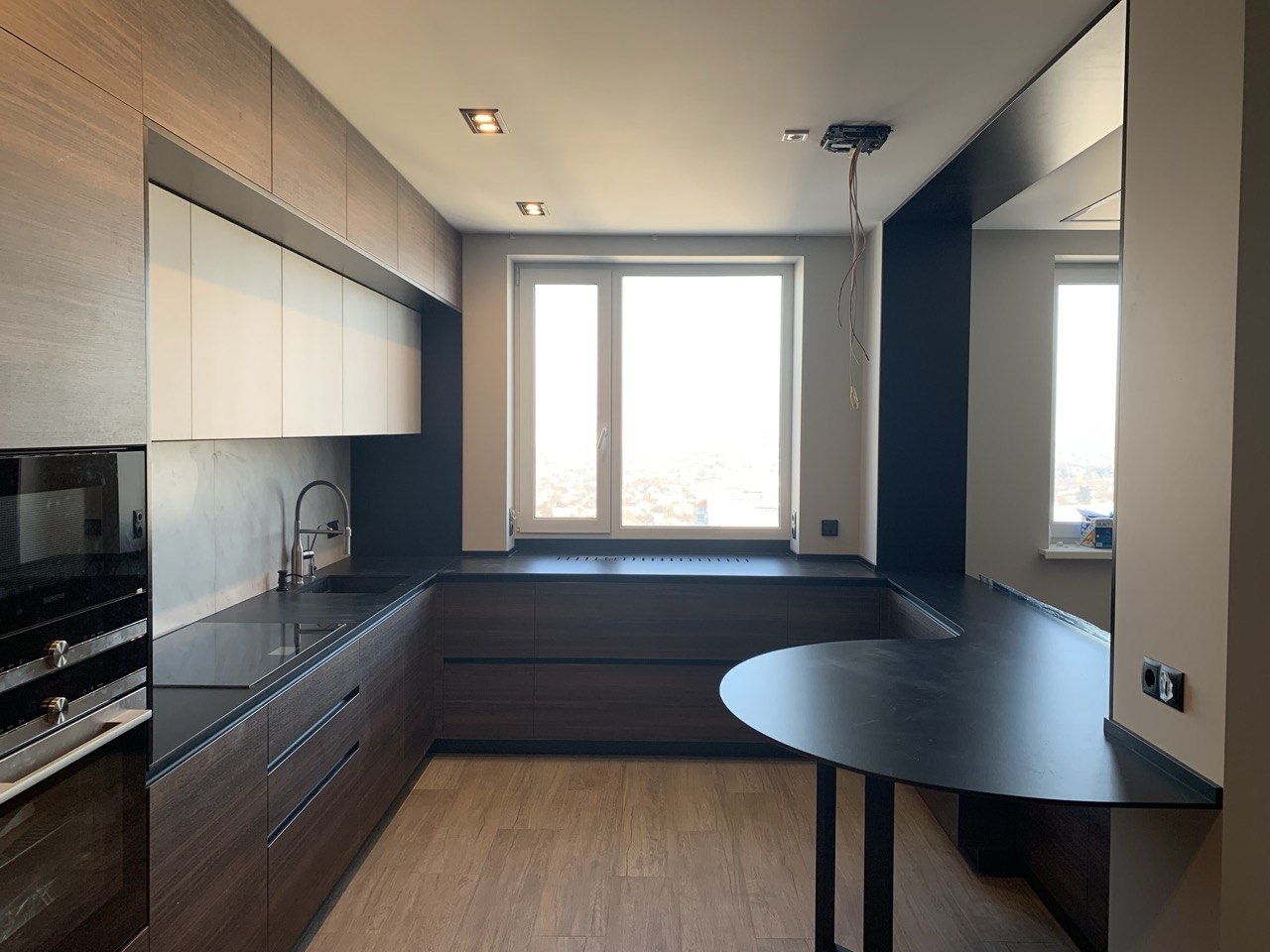Kuchnia w ciemnym fornirze z czarnym blatem i przedłużeniem blatu w stronę okna — realizacja Bellissimo Home.