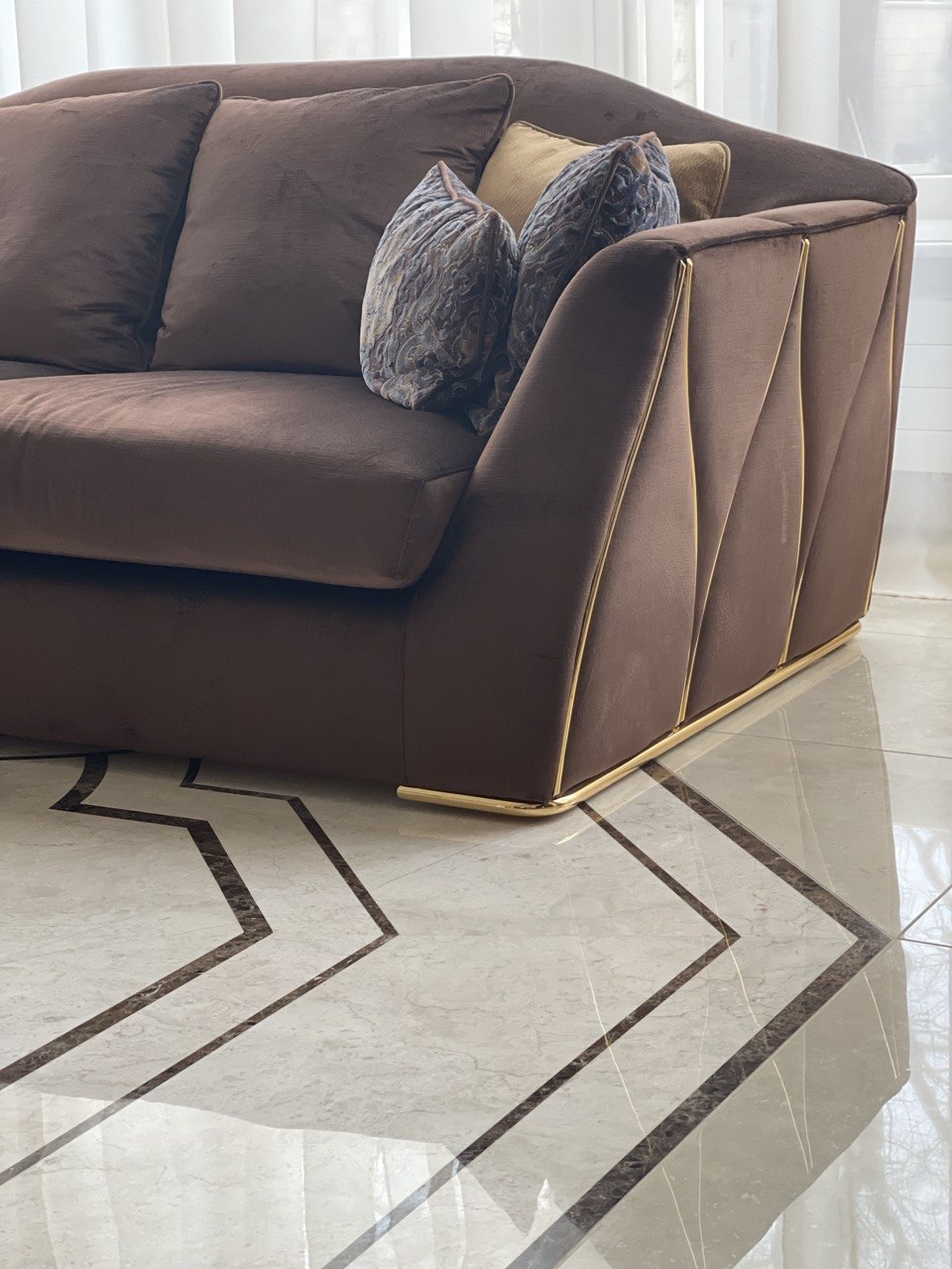 Brązowa sofa z weluru ze złotym cokołem, na marmurowej posadzce z dekoracyjną intarsją — realizacja Bellissimo Home.